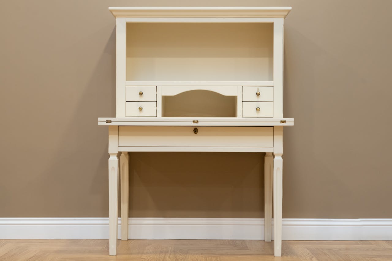 Minimalist cream wooden desk with drawers and shelf against a brown background.